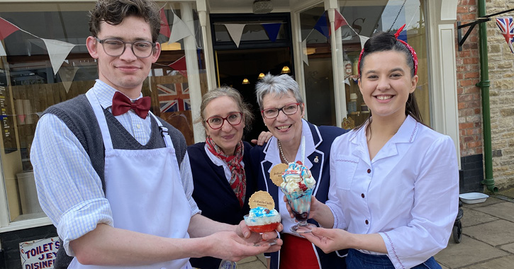 group of museum staff dressed in 1950s clothing holding ice creams outside of John's Café at Beamish Museum.